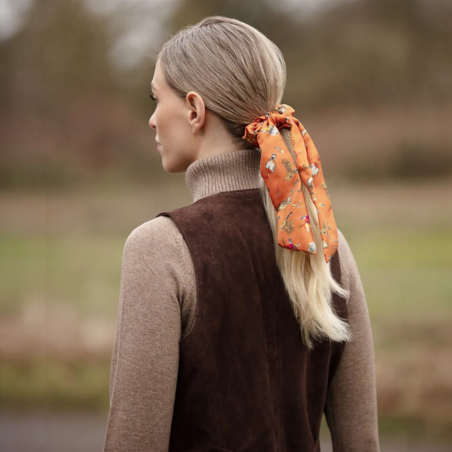 Woman with a ponytail wearing an orange scrunchie in a natural setting