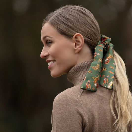 Woman with a patterned scrunchie in her hair, wearing a brown sweater outdoors.